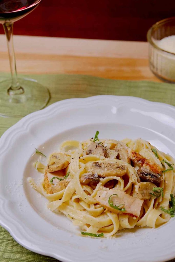 Light Chicken and Mushroom Fettuccine In white bowl set on green placemat with wine glass and grated cheese in background