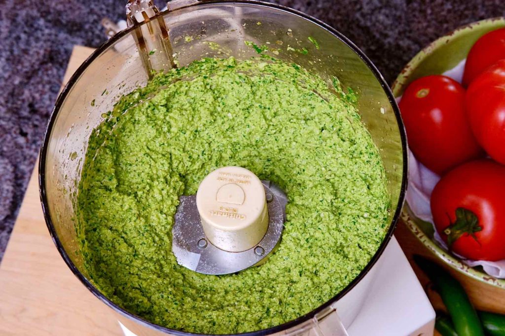 Jalapeno Pesto Sauce processed in a food processor with bowl of tomatoes in background>