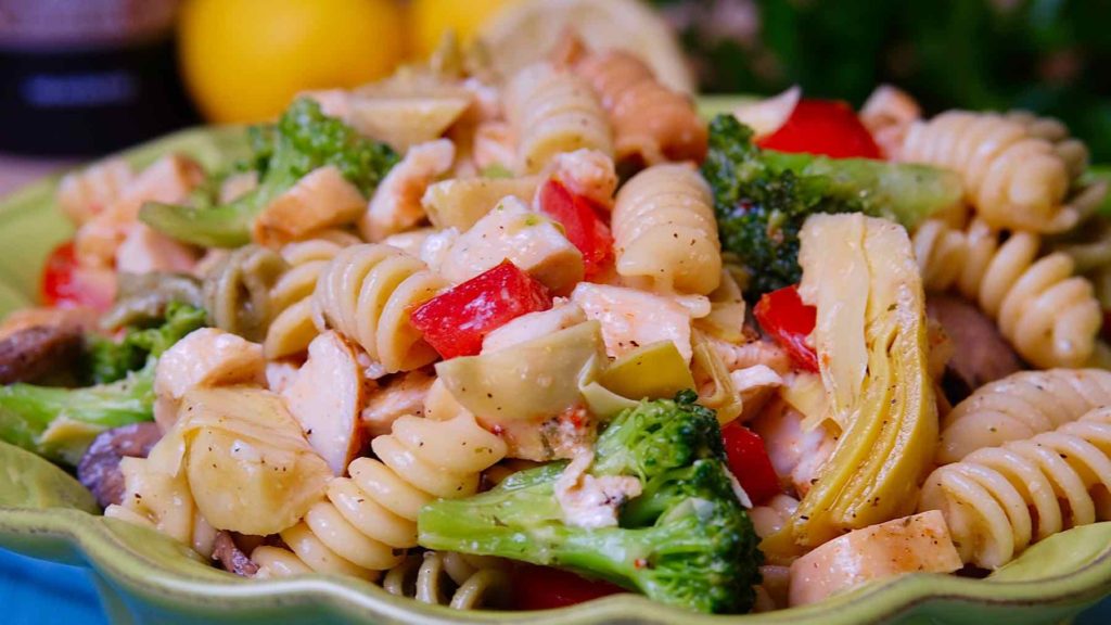 Pasta Salad dressed with Italian Style dressing in green serving bowl with lemons and parsley in background.
