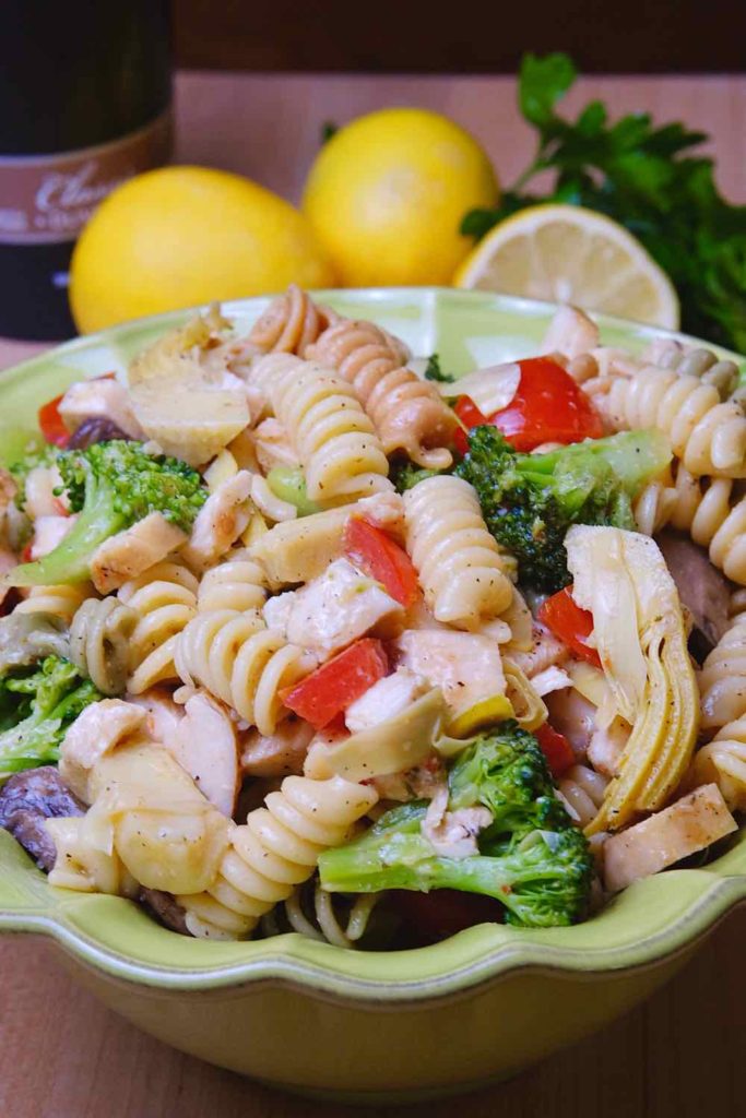 Italian Style Pasta Salad in green serving bowl, with lemons and olive oil in background.