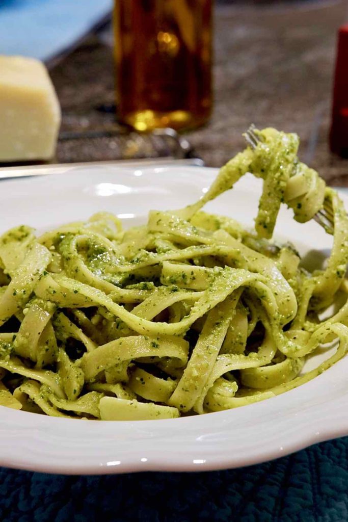 Pasta pesto made with Jalapeno Pesto in white bowl.  Fork with pasta wound around it and cheese and grater in background.