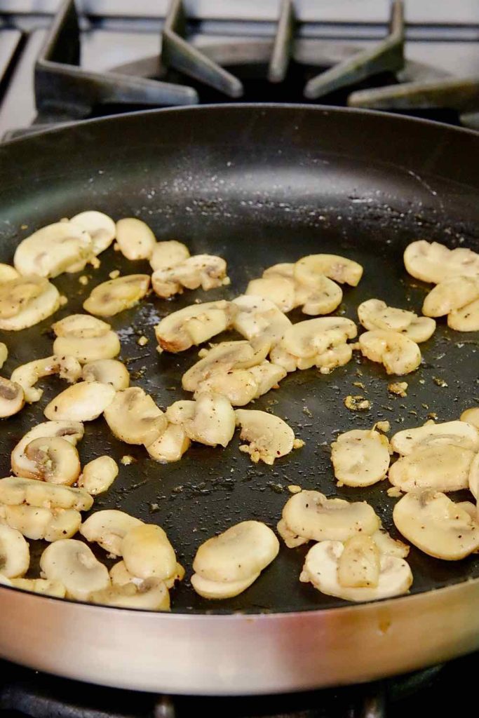 Sauteed Mushrooms in black nonstick skillett on stove top.  