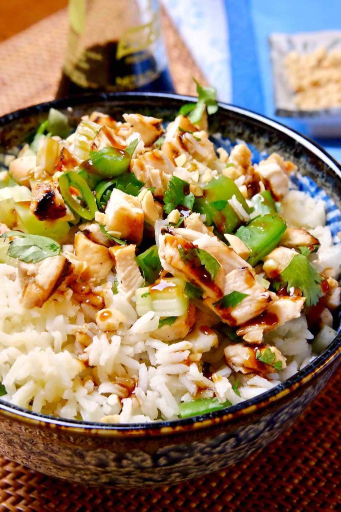 Hoisin Chicken Rice in a blue bowl set on a rattan mat with blue linen in background.