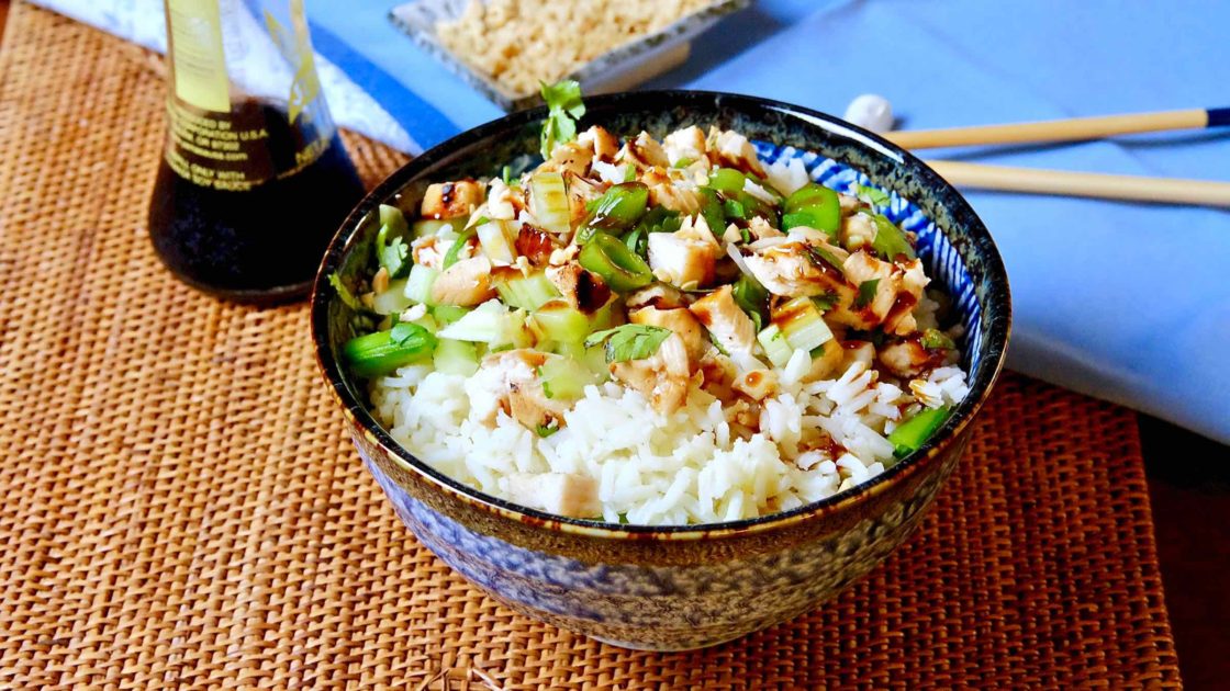 Hoisin Chicken with rice in Blue Japanese rice bowl set on rattan mat with blue linen and chopped peanuts in background.