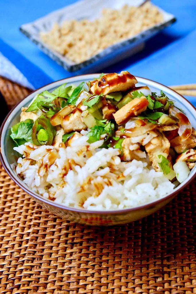 Healthy Hoisin Chicken Bowl with Rice is served in blue rice bowl set on rattan mat with blue linen in background.