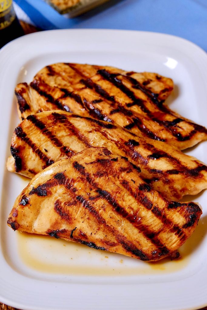 Grilled Hoisin Chicken Breasts resting on rectangular white plate with blue linen underlay.
