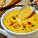 Corn Chowder served in a two handled soup bowl with spoon shot. Chowder is garnished with bell pepper, parsley and bacon bits.