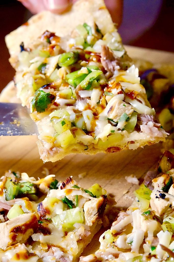 Hoisin Chicken Flatbread cut into pieces on maple cutting board.  One slice is lifted up on knife edge.