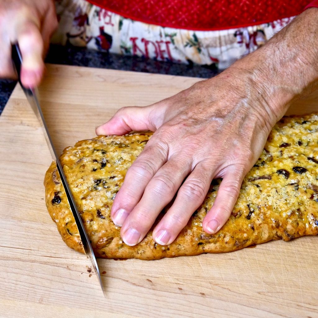 Baked log being cut into biscotti slices with serrated knife.