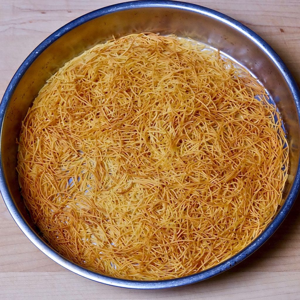 Baking pan with toasted noodles set on a maple wood bowl. 