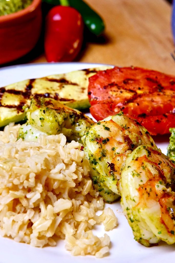 Shrimp rubbed with Spicy Jalapeno Pesto, brown rice and grilled vegetables on white plate.