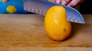 Fresh mango being cut on maple board.