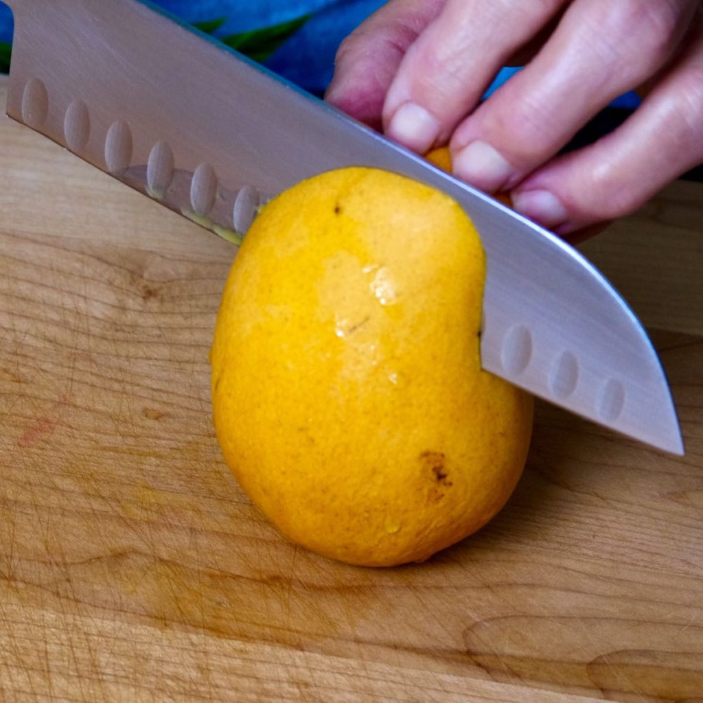 Mango being cut away from pit on maple board.