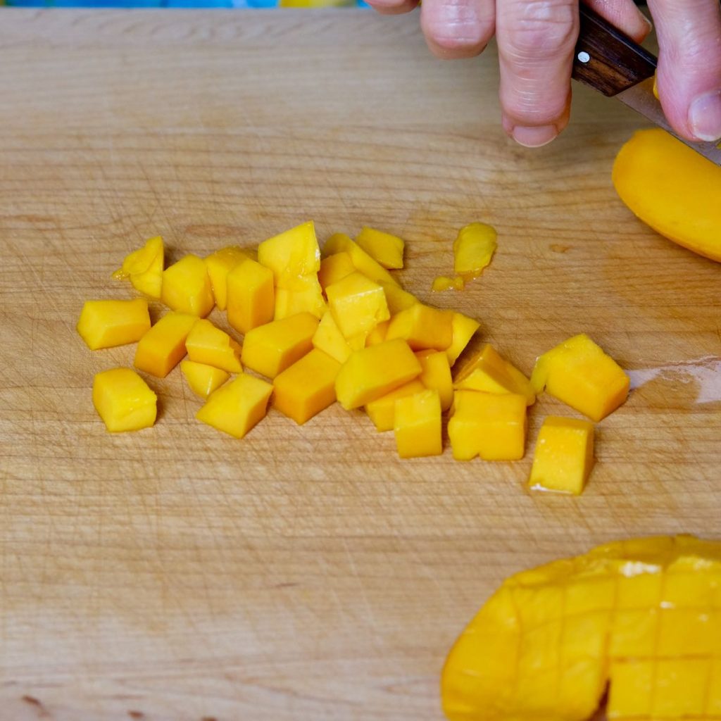 Freshly cut mango cubes on maple wood board.