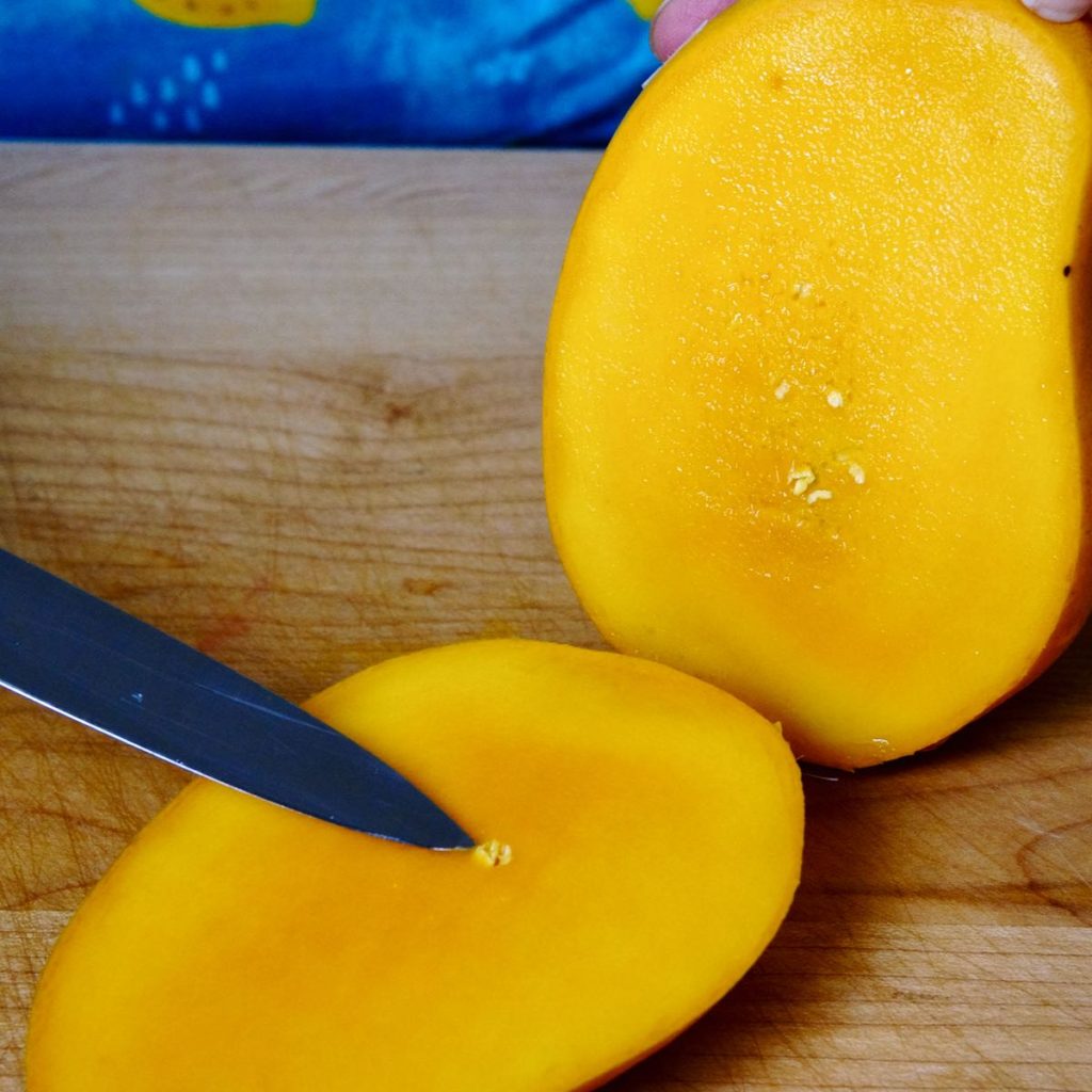 Cut mango with knife pointing to pit fibers.