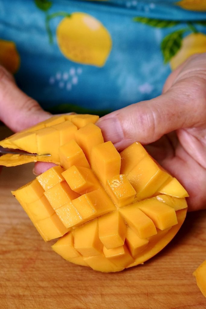 Cutting a mango into cubes over maple board.