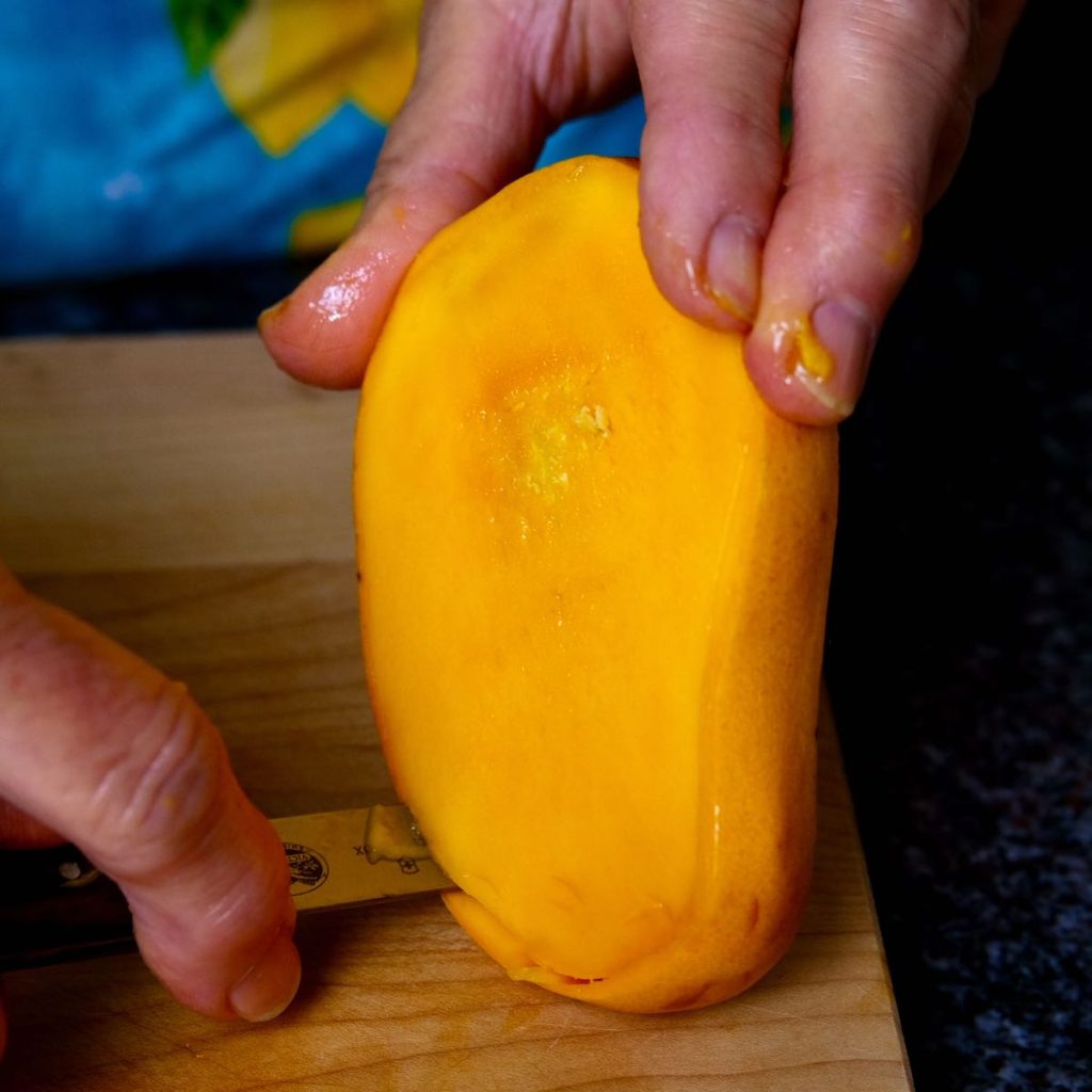 Mango pit being trimmed from the skin with pairing knife.