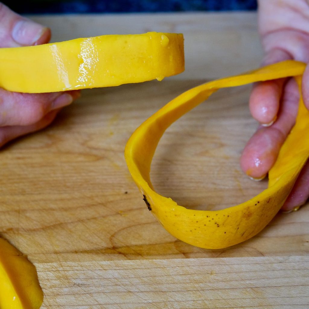 Rim of skin being removed from mango pit with maple board in background.