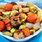 Grilled Panzanella Salad served in white bowl set on a turquoise charger plate