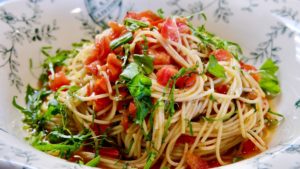 Whole wheat pasta served with fresh tomato sauce (Caprese style) in white and green Italian bowl garnished with shredded basil.