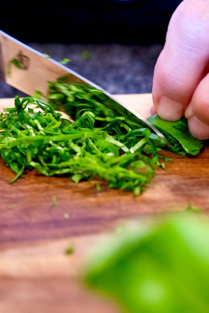 Shredded ribbons of basil being cut on a walnut board.