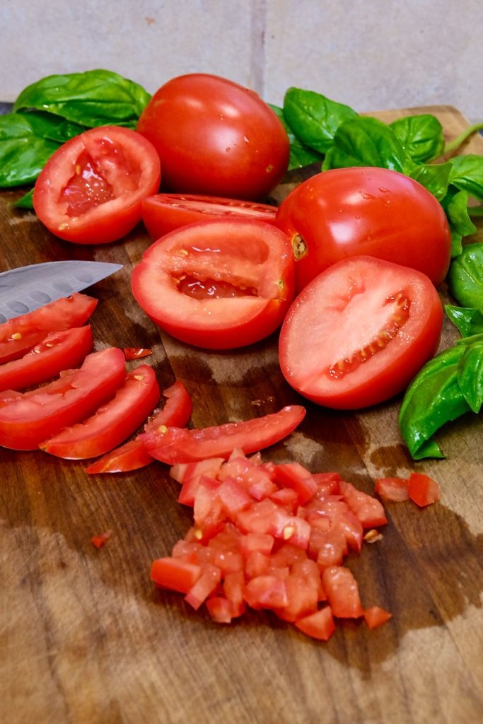 Roma tomatoes cut in half, halves made into slices and sliced cut into evenly diced pieces are displayed on walnut cutting board.