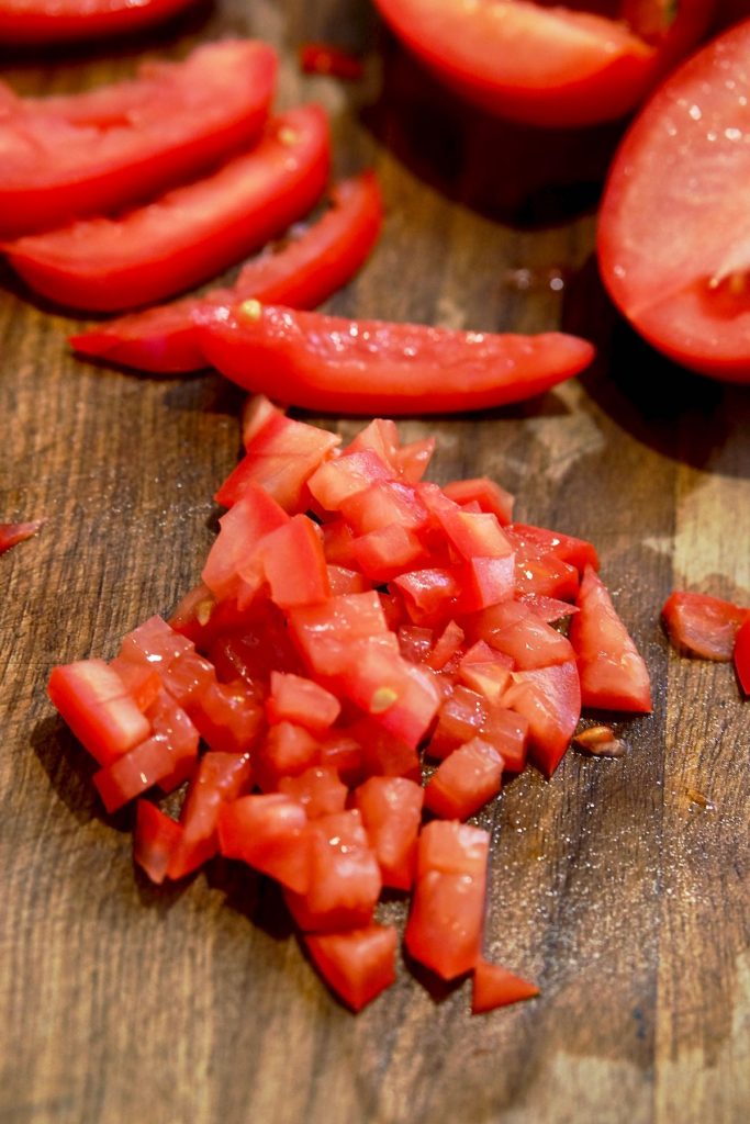 Roma tomatoes cut in half, halves made into slices and sliced cut into evenly diced pieces are displayed on walnut cutting board.