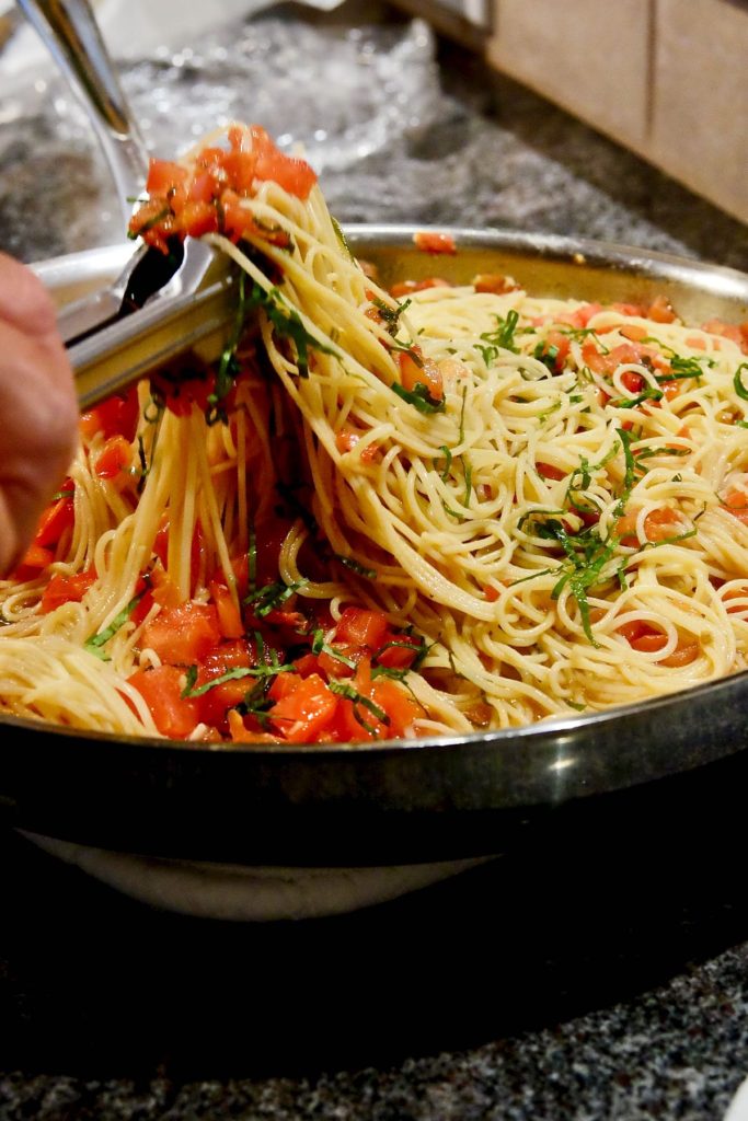Linguine alla Caprese in stainless steel pan being served into a pasta bowl.
