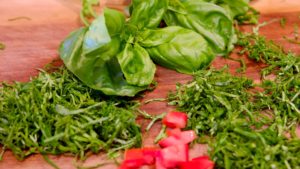 Walnut cutting board with a bouquet of whole basil in background with chiffonade basil in foreground with diced tomatoes.