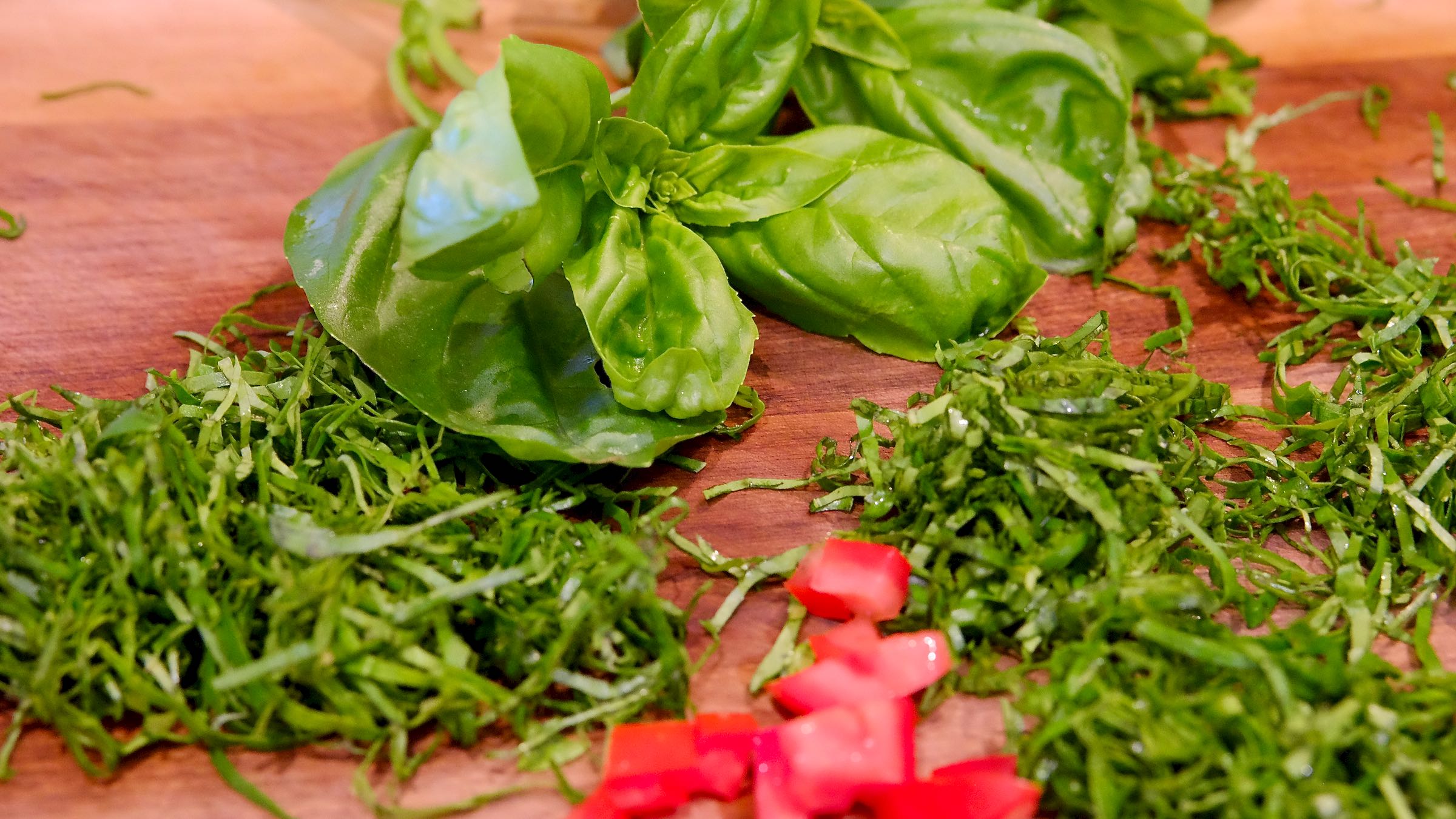 Walnut cutting board with a bouquet of whole basil in background with chiffonade basil in foreground with diced tomatoes.