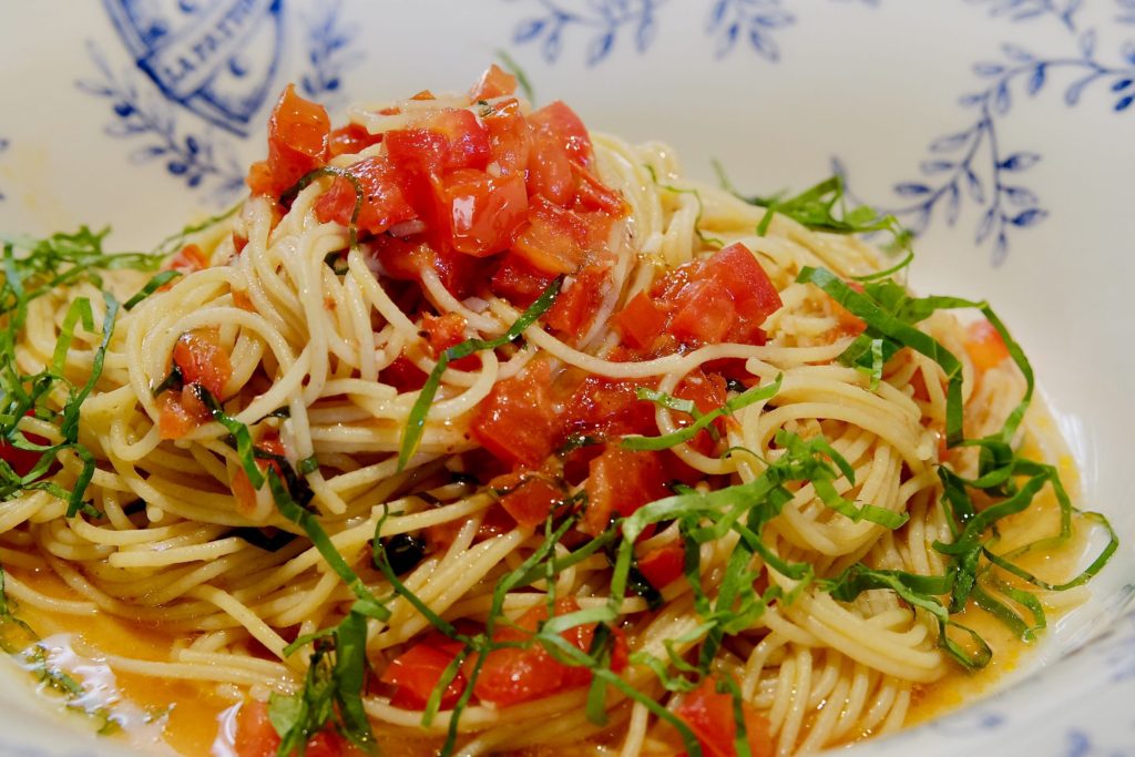 Linguine pasta served with fresh Caprese tomato sauce and garnished with basil chiffonade in blue and white pasta bowl.