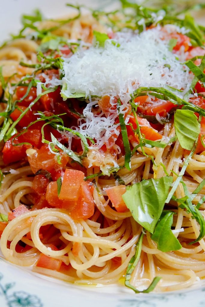 Linguine pasta with fresh tomato sauce garnished with basil chiffonade and Romano cheese served and white and blue pasta bowl.