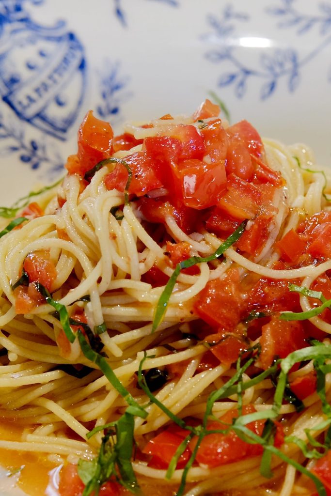 Linguine pasta with fresh tomato sauce garnished with basil chiffonade served in white and blue pasta bowl.