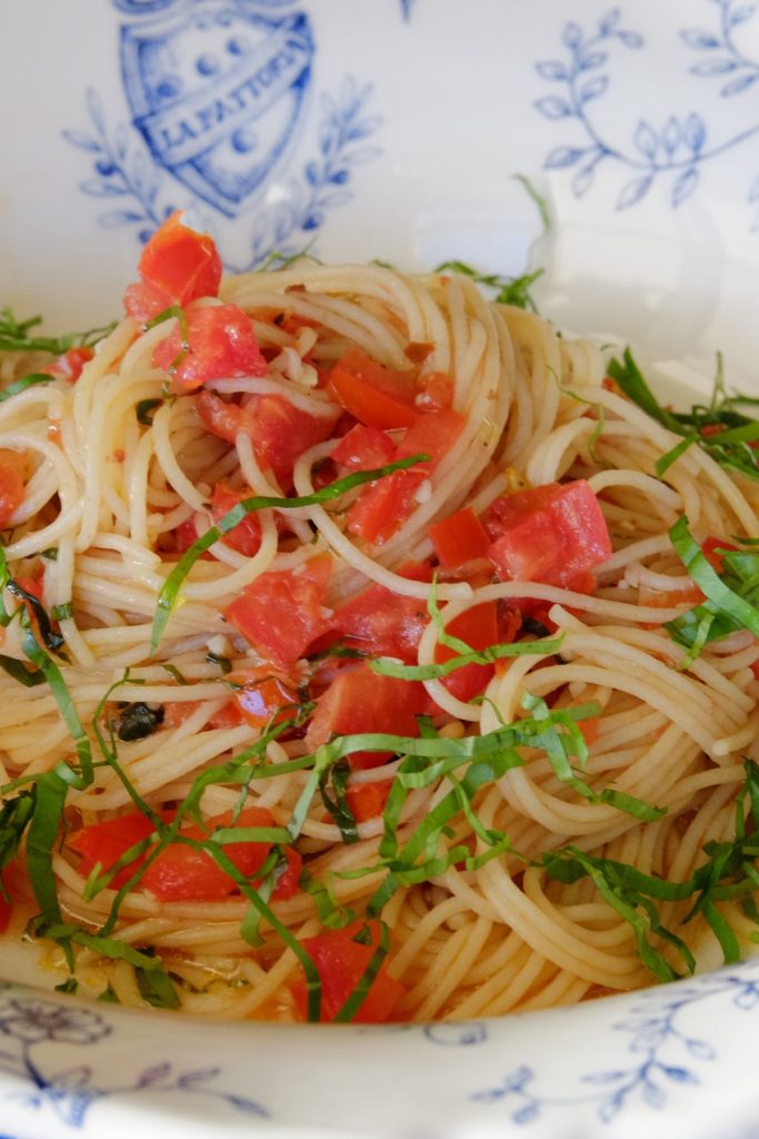 Linguine all Caprese garnished with basil chiffonade in blue and white Italian pasta bowl.