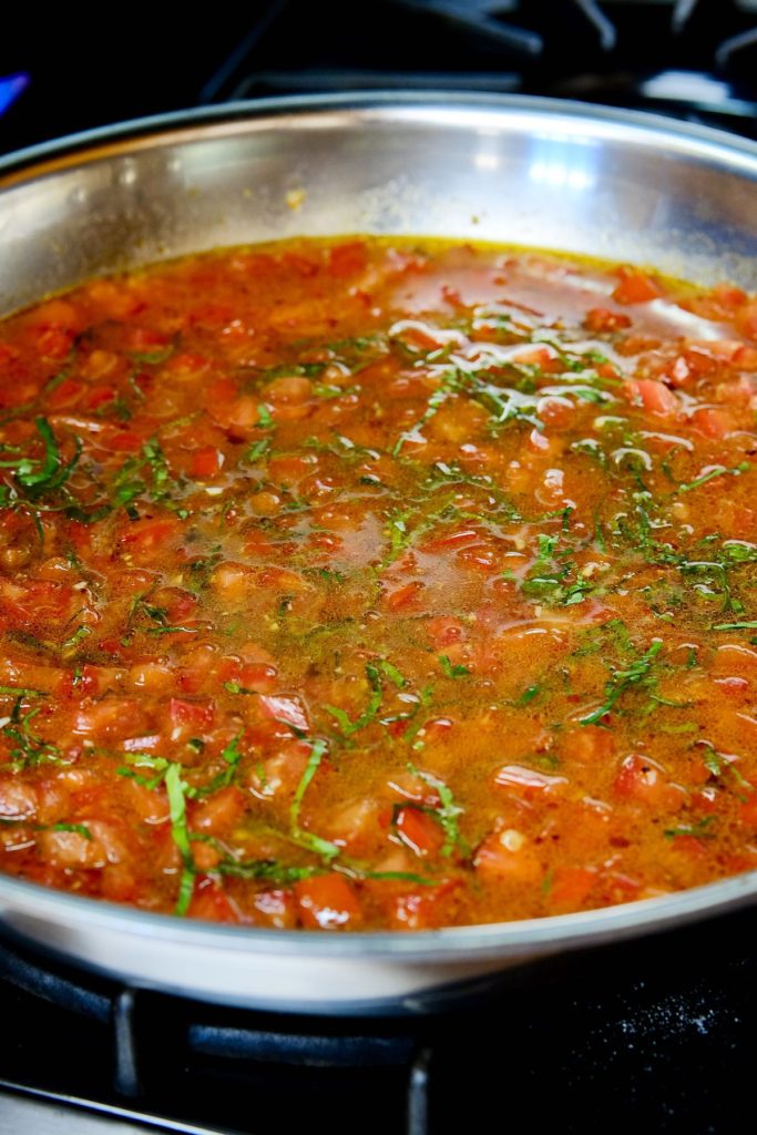 Basil Chiffonade added to  fresh tomato sauce cooking in stainless skillet.