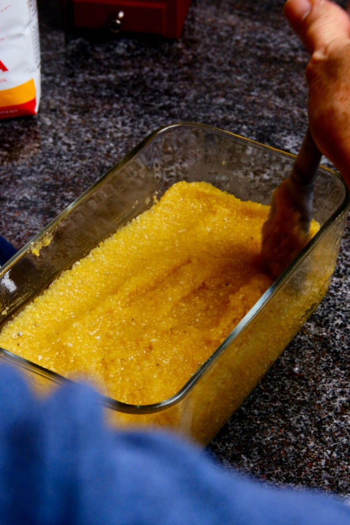 Leftover polenta being smoothed evenly into glass storage container.