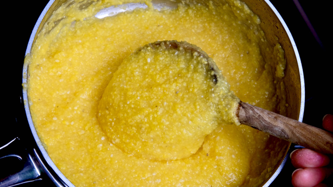 Basic Polenta being stirred in a stainless steel pot with an olive wood spoon.