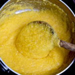 Basic Polenta being stirred in a stainless steel pot with an olive wood spoon.