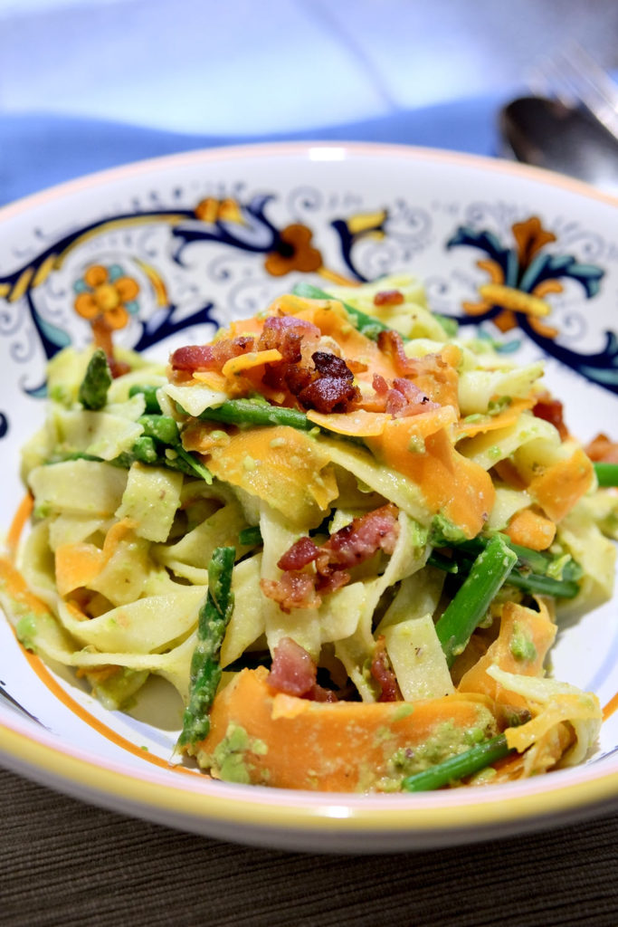 Pasta primavera with Pea and pistachio pesto sauce served in a multi-colored Italian pasta bowl .  Pasta is garnished with bacon bits.