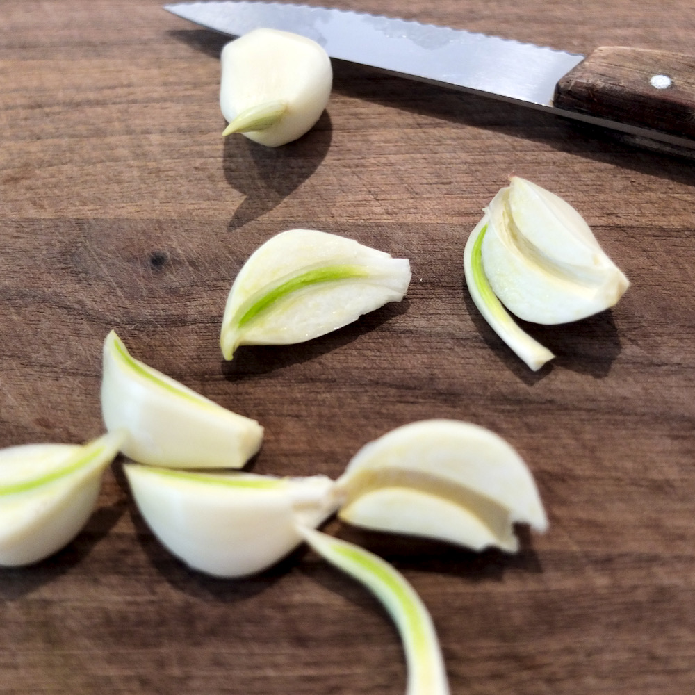 Fresh garlic cloves peeled and cut in half on walnut cutting board with knife in background.  Picture depicts removal of sprout removed from garlic center.