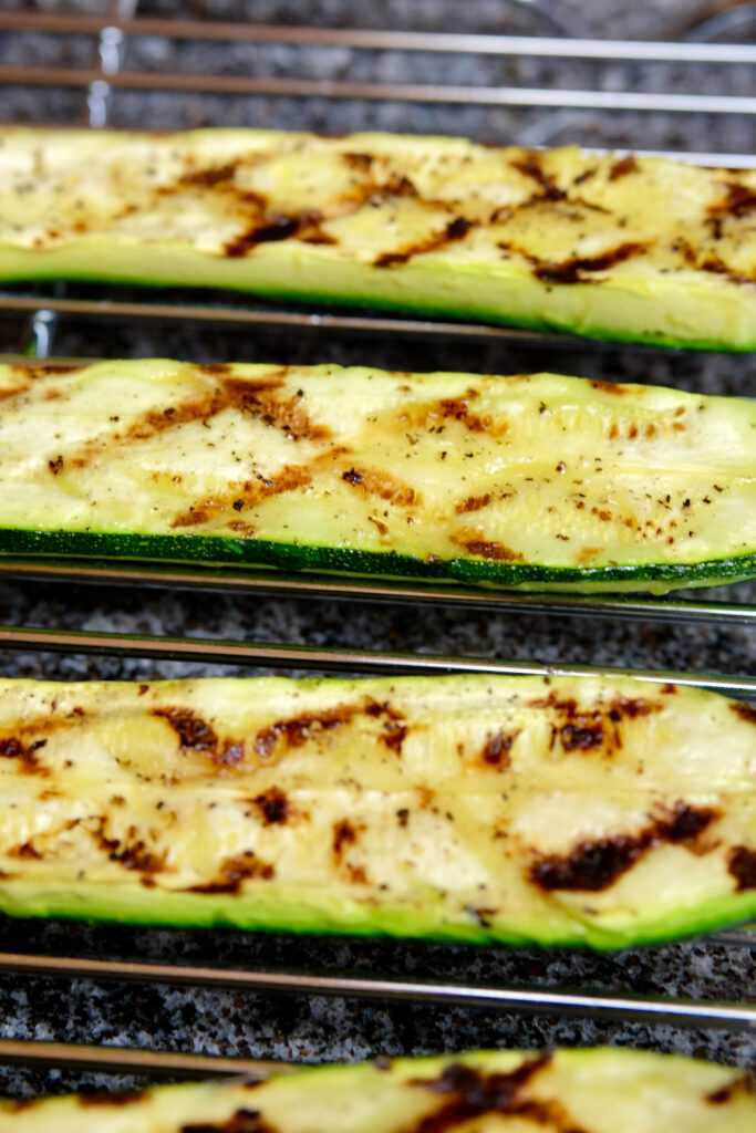 Grilled zucchini halves cooling on wire rack set over granite countertop.