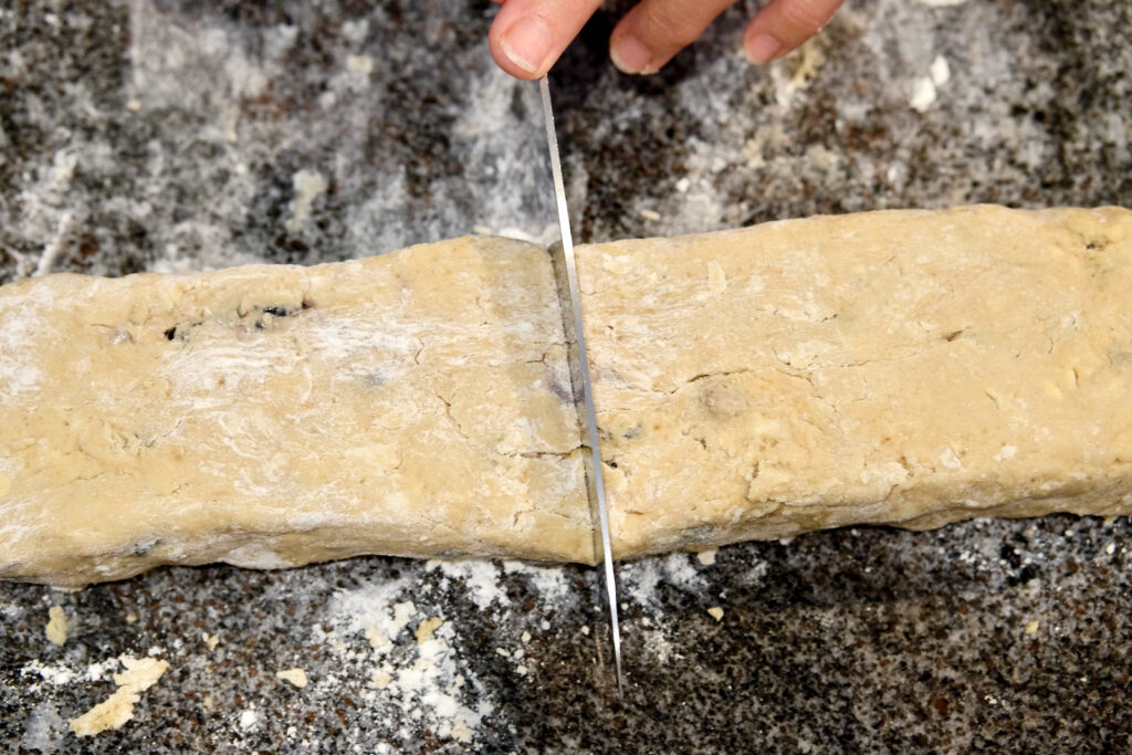 Dough log on floured marble surface showing knife cutting 12-inch log into two 6-inch pieces.