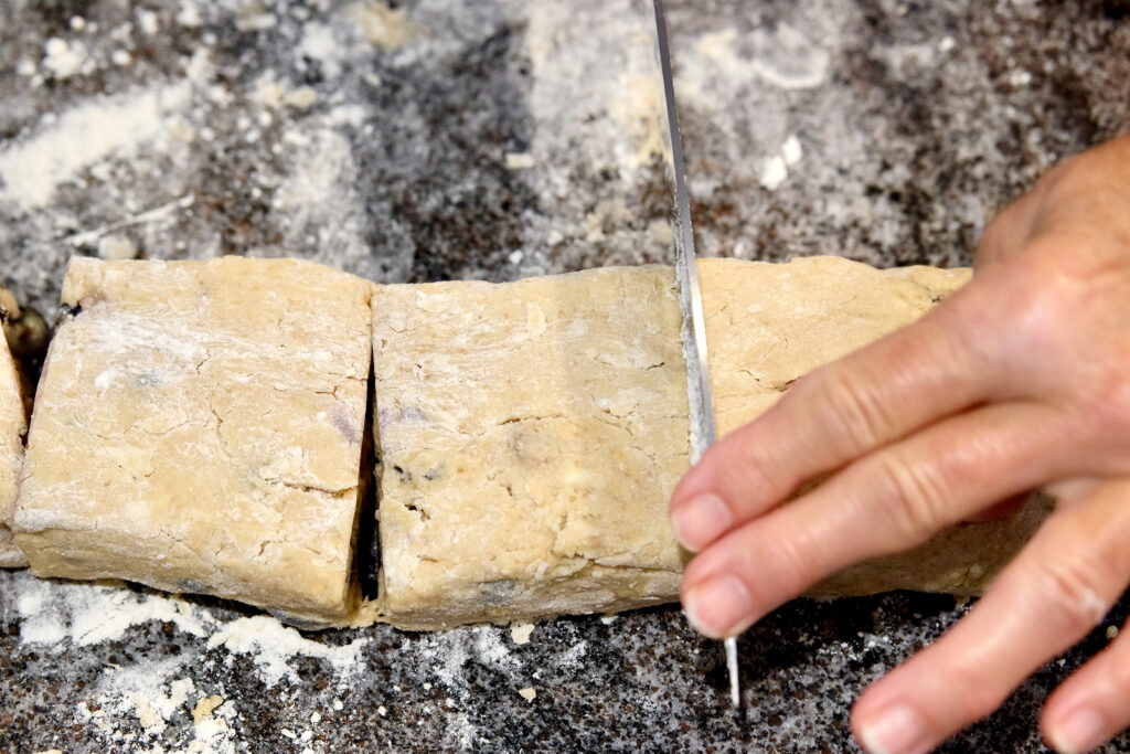 Dough pieces on floured marble surface showing knife cutting 6-inch pieces in have to create a two squares.