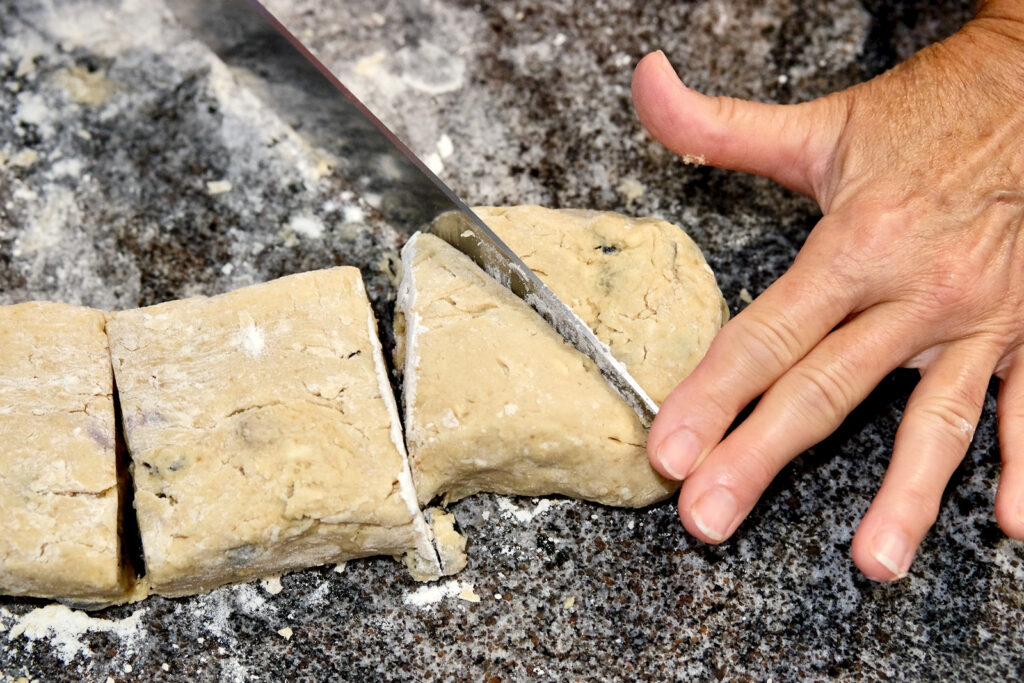 Dough on floured marble surface showing knife cutting each square into wedges. 