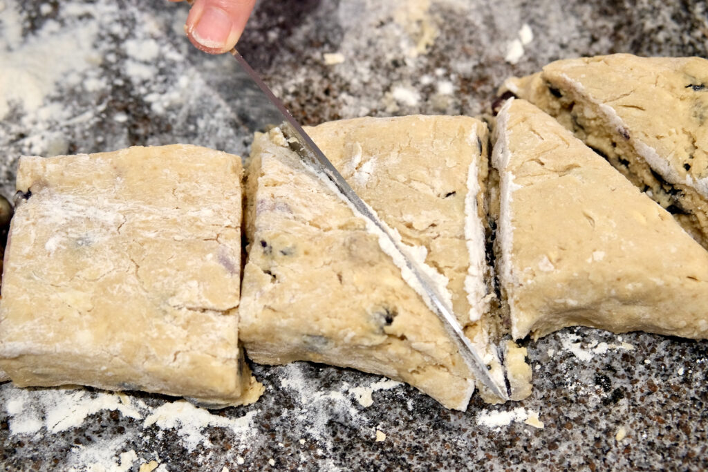 Dough on floured marble surface showing knife cutting each square into 8 equal wedges .