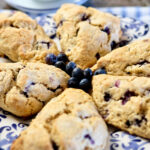 Oatmeal and Blueberry Scones arranged on a blue and white Italian plate with cluster of fresh blueberries in center.