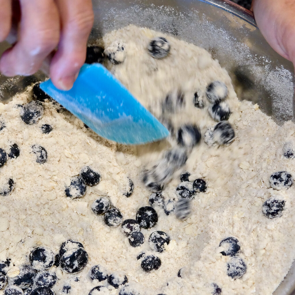 Mixing berries into dry ingredient in a stainless steel bowl.