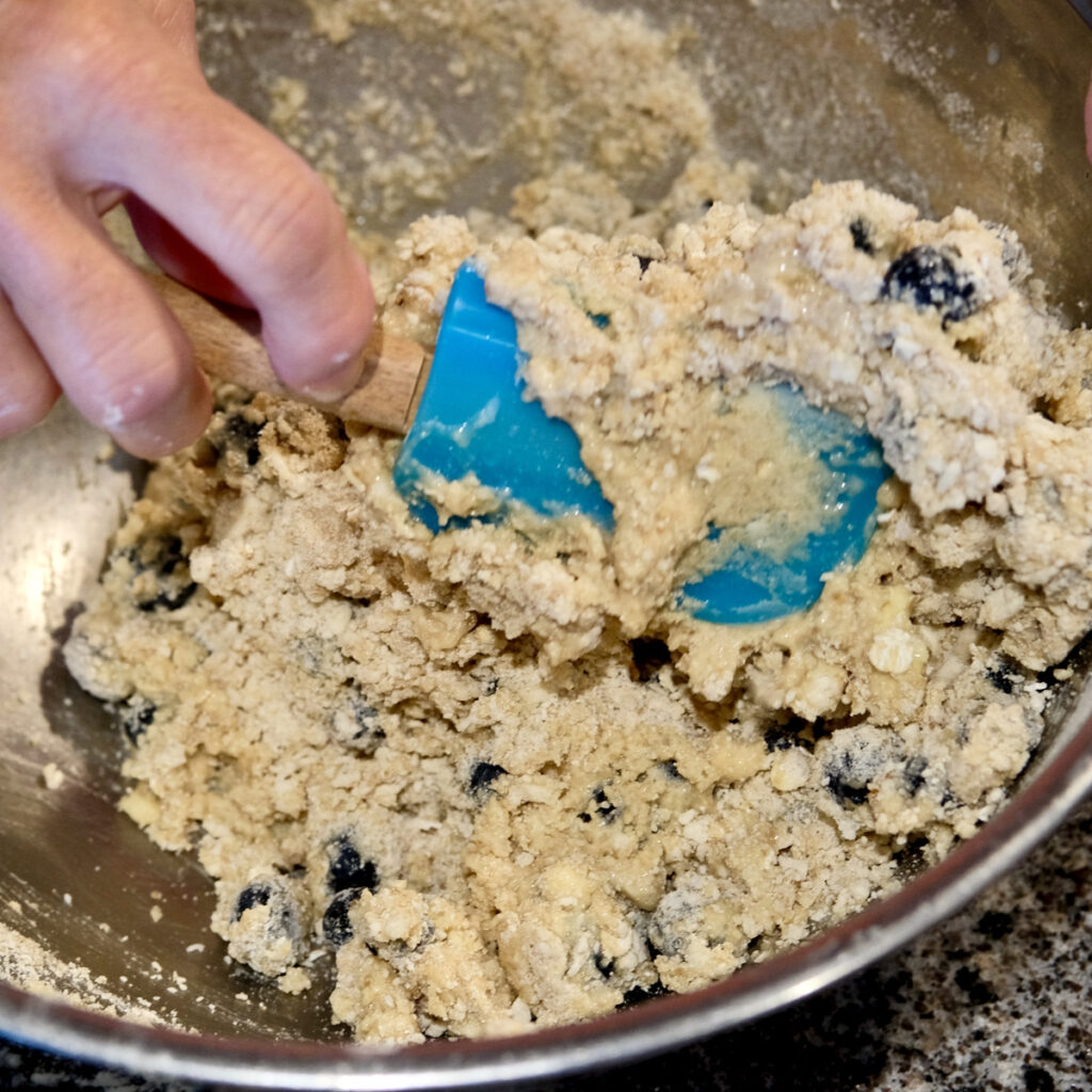 Hand holding blue spatula showing the texture of folded ingredients.