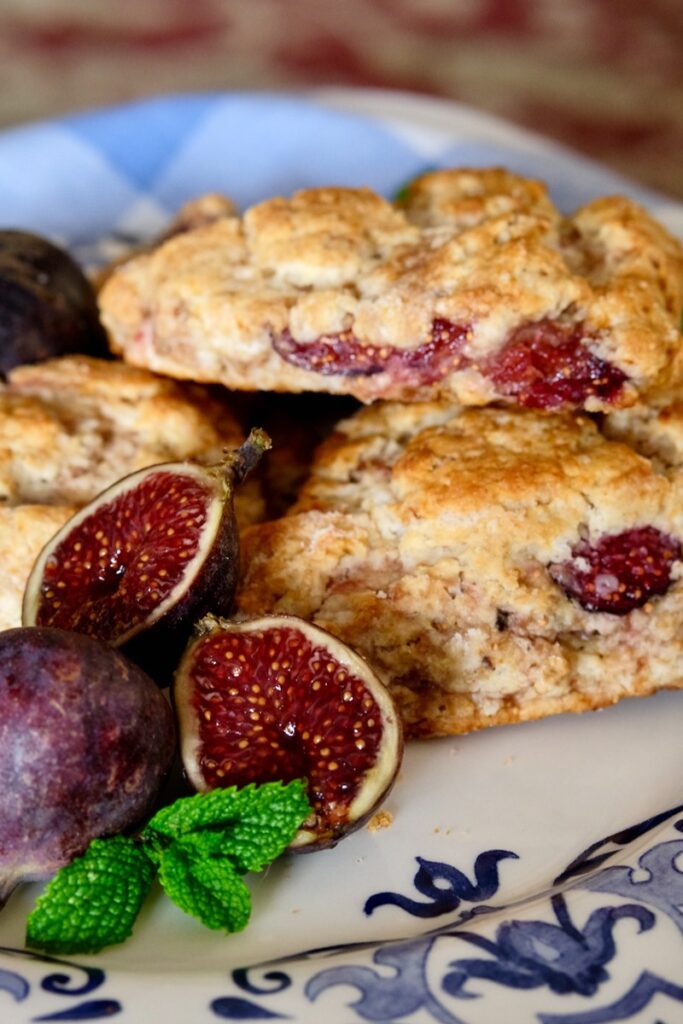 Fresh fig scone plated on white and blue Italian plate with whole and cut figs in forefront.