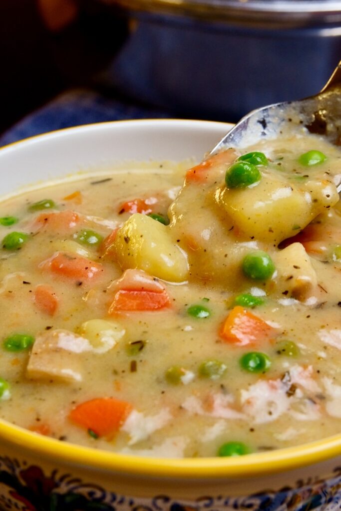 A multi colored soup bowl filled to the brim with chicken pot pie soup while a spoonful hovers over the bowl.